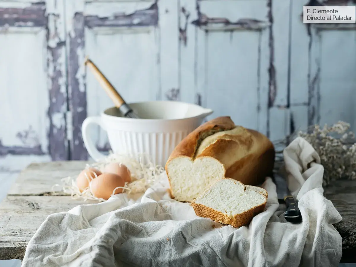 Pan brioche para torrijas, huevos y batidor sobre mesa rústica.