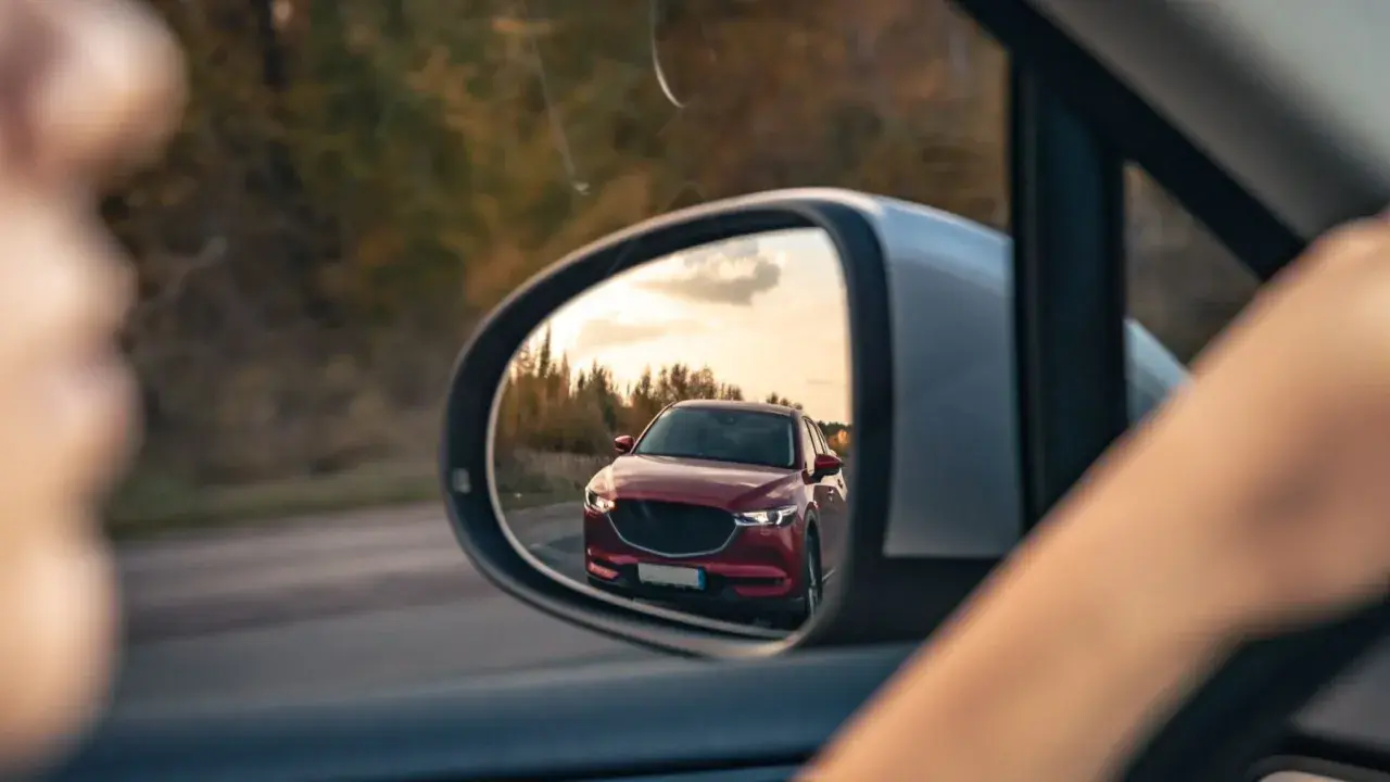 Reflejo de un coche rojo en el espejo retrovisor, preparándose para un adelantamiento. DGT.
