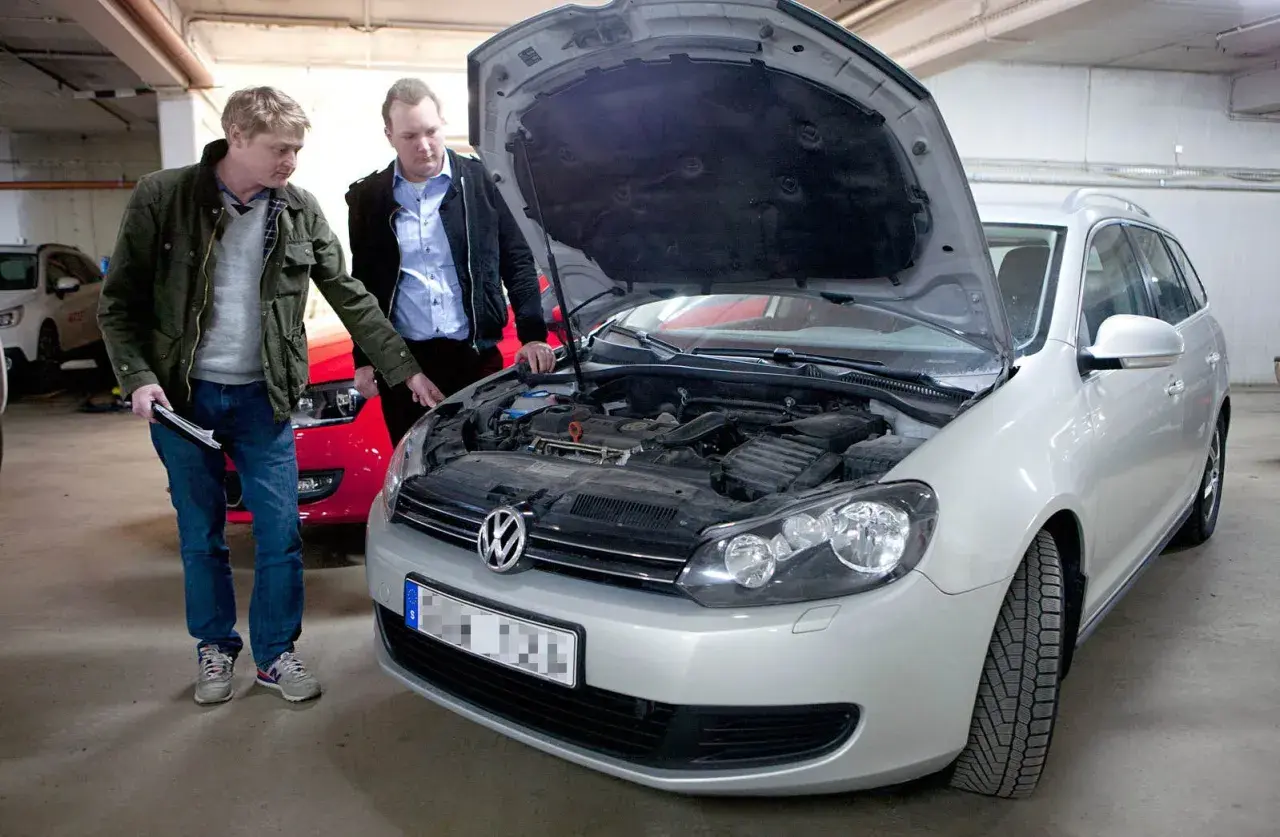 Två män inspekterar motorutrymmet på en silverfärgad kombi. En av dem pekar mot motorn, kanske för att diskutera kamremmen på 1.4 TSI-motorn.