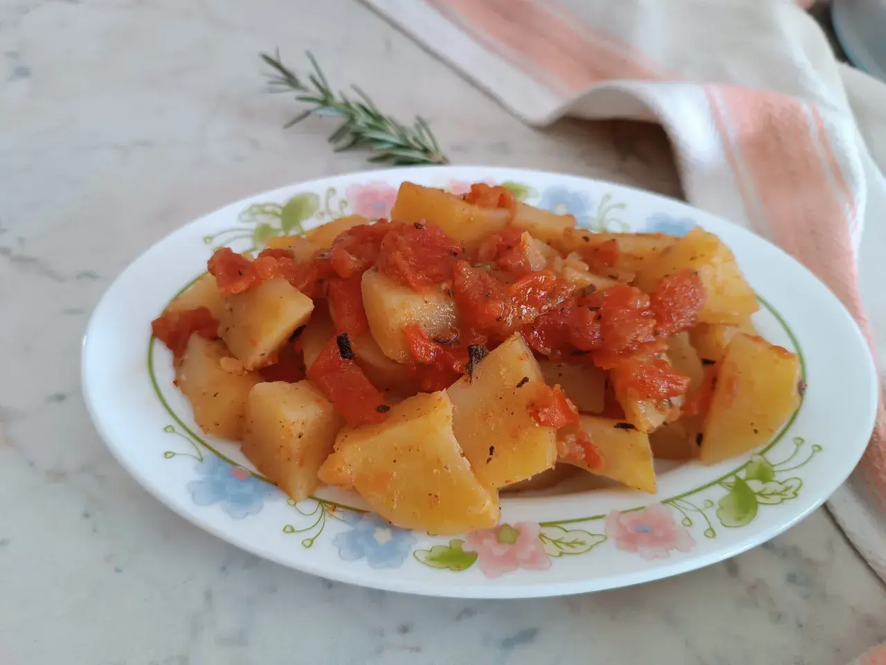 Patate in umido con pomodoro e rosmarino, un piatto semplice e gustoso, servito su un piatto fiorato.