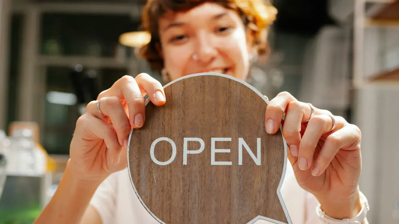 Frau hält ein Holzschild mit der Aufschrift "OPEN" in einem Café.