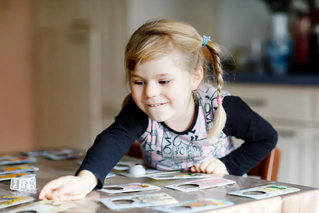 Niña rubia con coletas jugando a un juego de memoria infantil, concentrada en las cartas sobre la mesa.