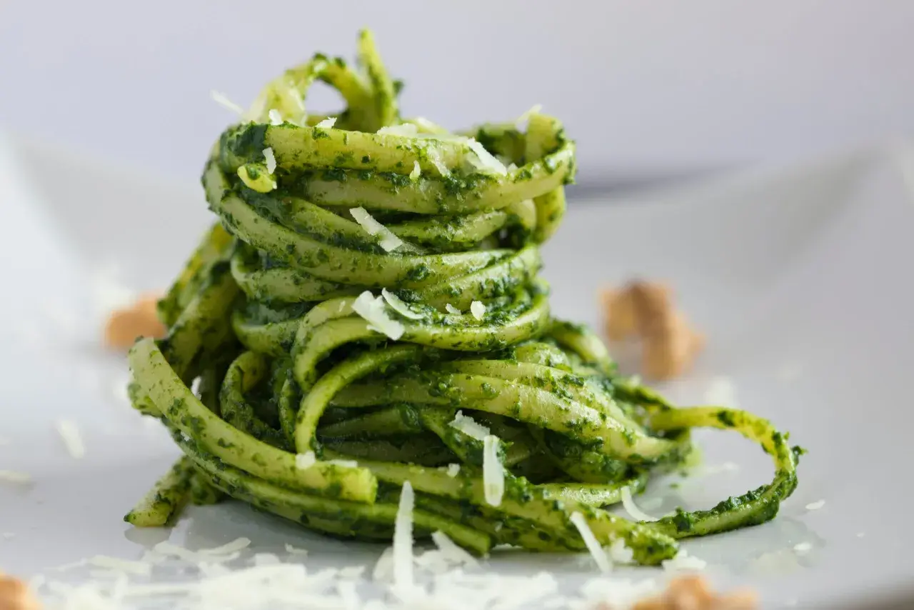 Makaron tagliatelle z zielonym pesto bazyliowym i startym parmezanem na białym talerzu.