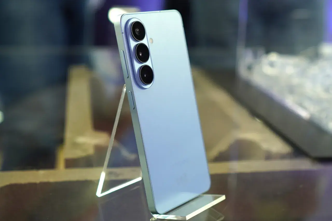 Jasnoniebieski Samsung Galaxy S26 z potrójnym aparatem z tyłu, stojący na przezroczystej podstawce.