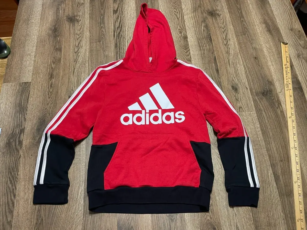 Czerwona bluza z kapturem Adidas dla chłopca z białym logo i czarnymi wstawkami.