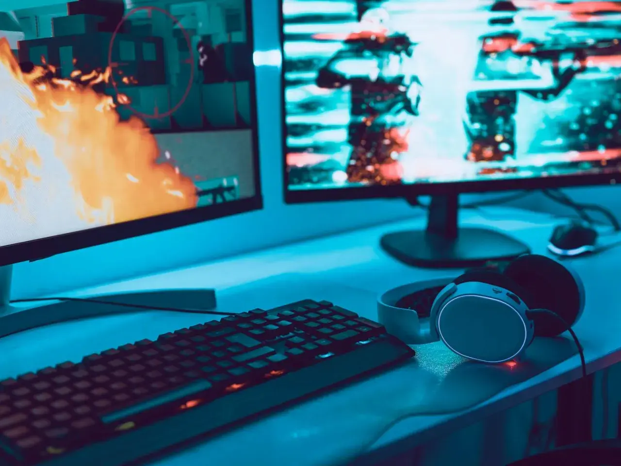 Gaming-Setup mit zwei Monitoren, Tastatur und Kopfhörern. Auf dem linken Bildschirm lodert Feuer, rechts sind Charaktere zu sehen. Perfekt für VA oder IPS.