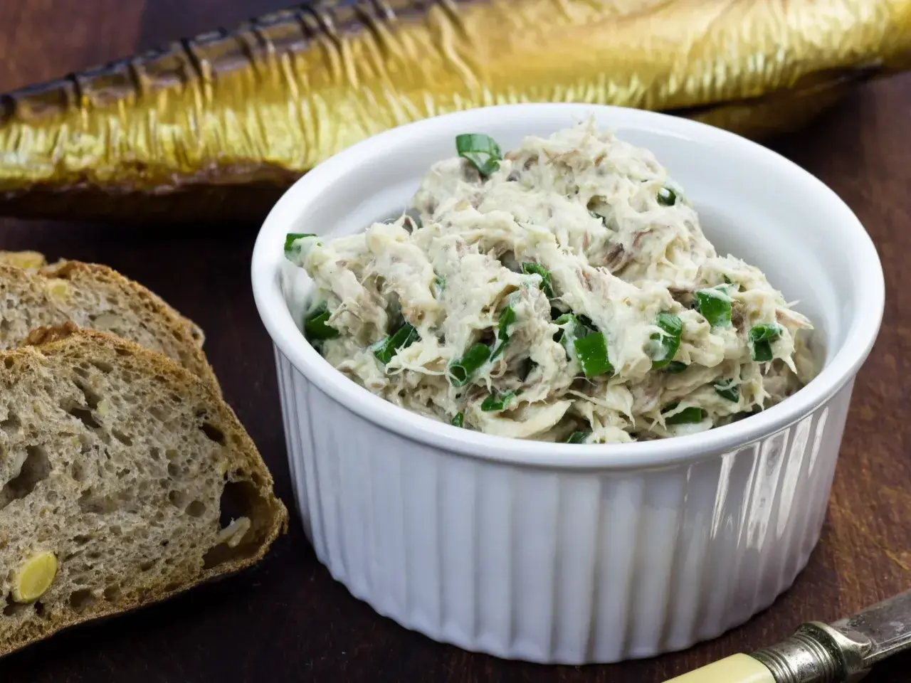 Pyszna pasta z makreli i twarogu, posypana szczypiorkiem, obok kromek chleba i wędzonej makreli.