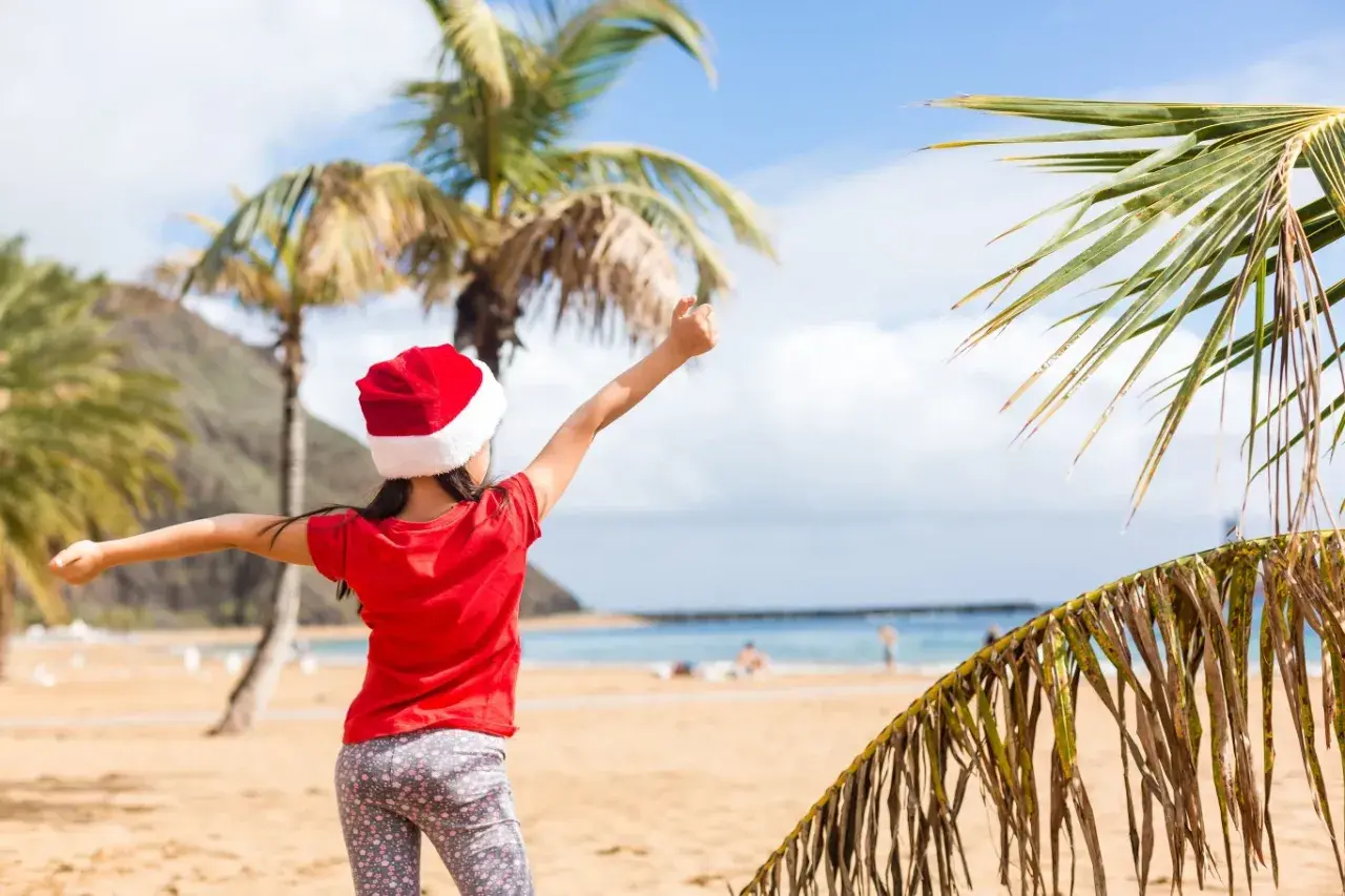 Dziewczynka w czapce Mikołaja cieszy się plażą i palmami. To wyjątkowe boże narodzenie w ciepłych krajach, gdzie śnieg zastępuje piasek.