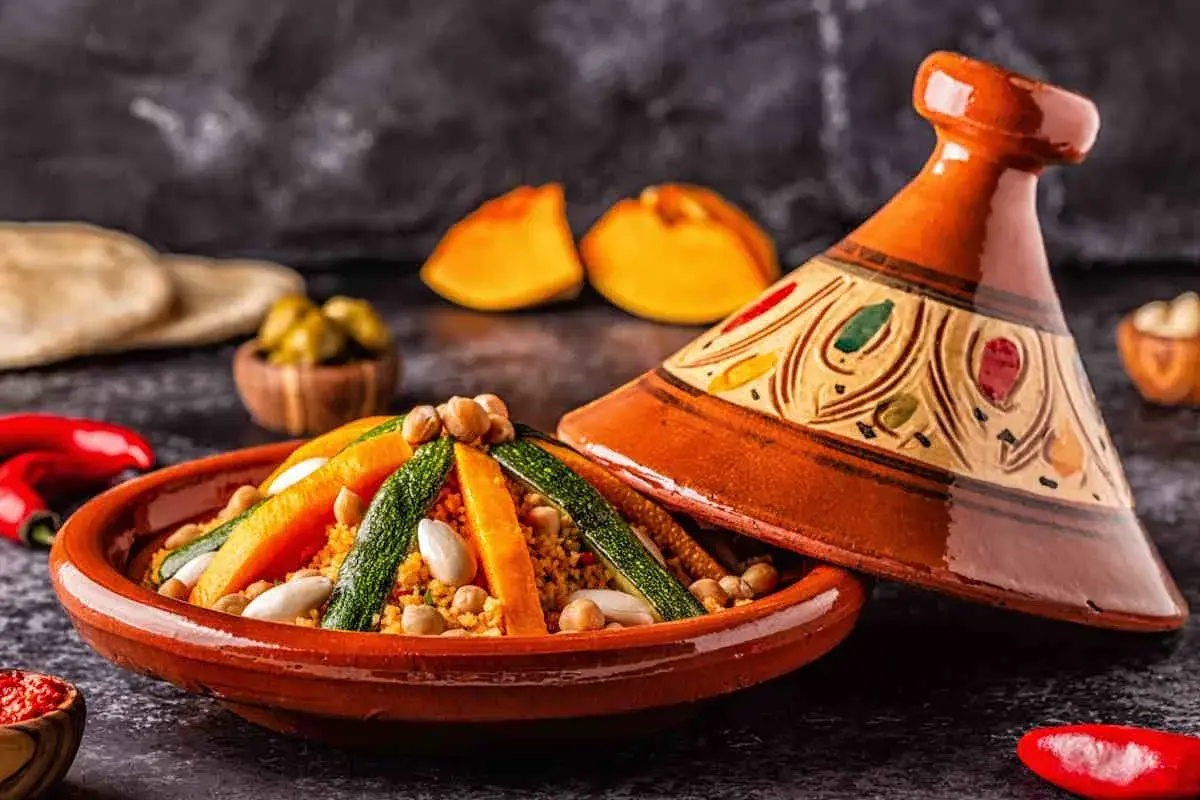 Un saporito cous cous tajine con verdure colorate e ceci, servito in un tradizionale piatto di terracotta decorato.