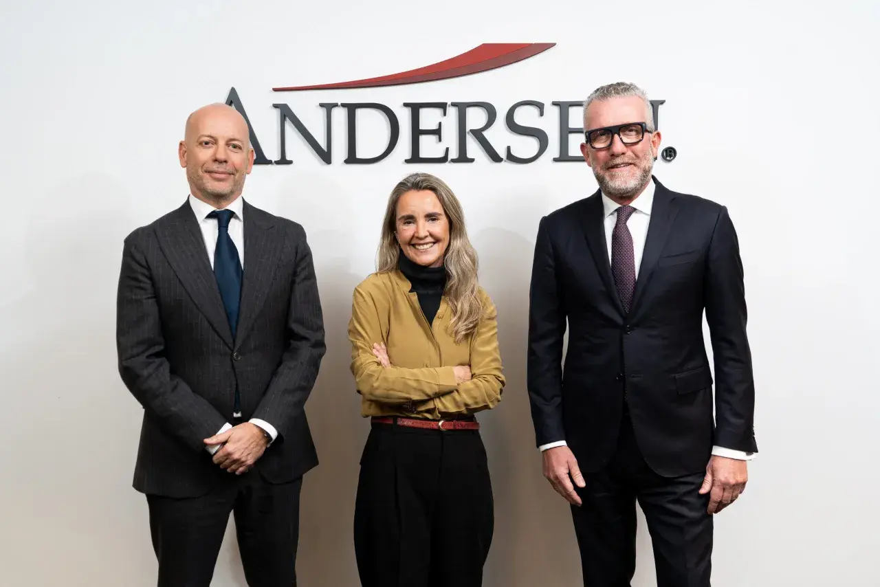 Tres personas posan frente al logo de Andersen. El hombre de la izquierda, calvo, viste traje gris. La mujer del centro, con brazos cruzados, lleva una blusa ocre. El hombre de la derecha, con gafas, viste traje oscuro. Un momento clave, como un ejempl...