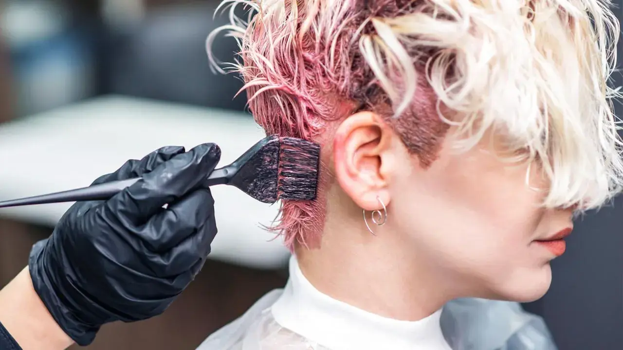 Manos enguantadas aplican tinte rosa al cabello. Si te manchas, aprende como quitar el tinte de la piel.