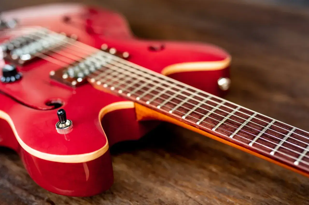 Czerwona gitara elektryczna na drewnianym tle. Idealna do nauki gry na gitarze elektrycznej.