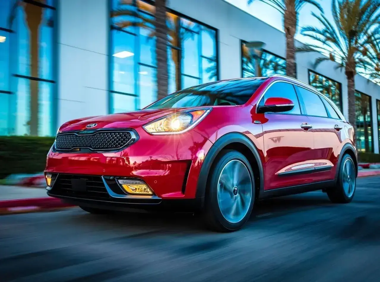Czerwony Kia Niro Hybrid w ruchu, z palmami i nowoczesnym budynkiem w tle.