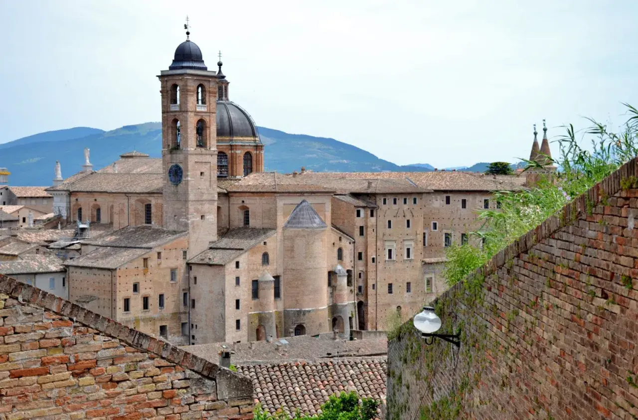 La maestosa corte di Urbino, con il suo campanile e la cupola, si staglia contro le colline.