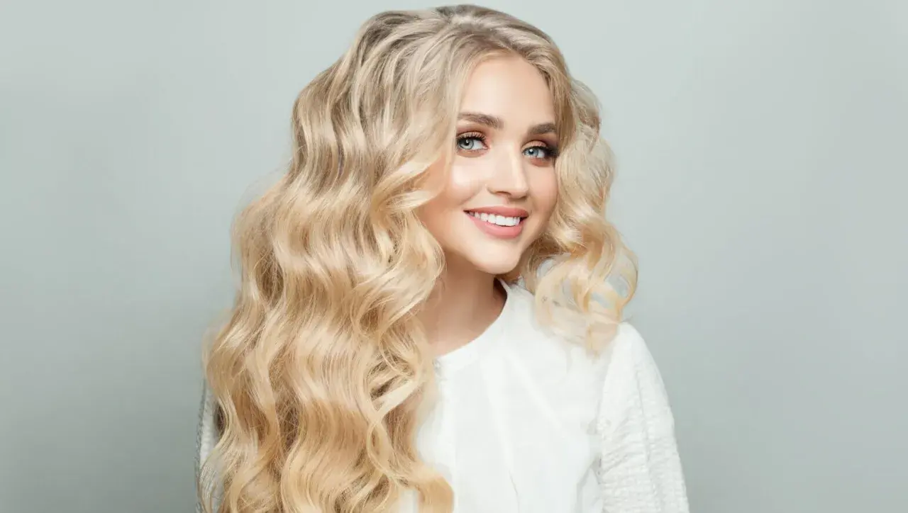 Mujer sonriente con cabello rubio mantequilla ondulado y ojos azules brillantes.