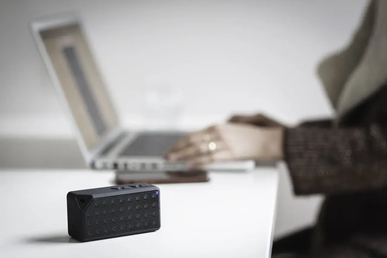 Mały głośnik z niebieską diodą obok laptopa. Dowiedz się, jak sprawdzić, czy komputer ma Bluetooth.