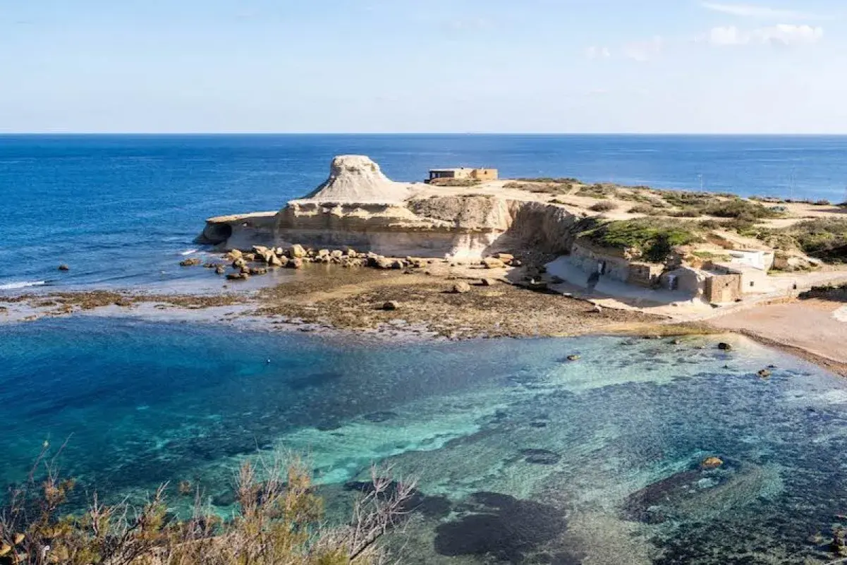 Felsige Küste mit kristallklarem Wasser und kleinen Gebäuden auf der Insel Gozo.