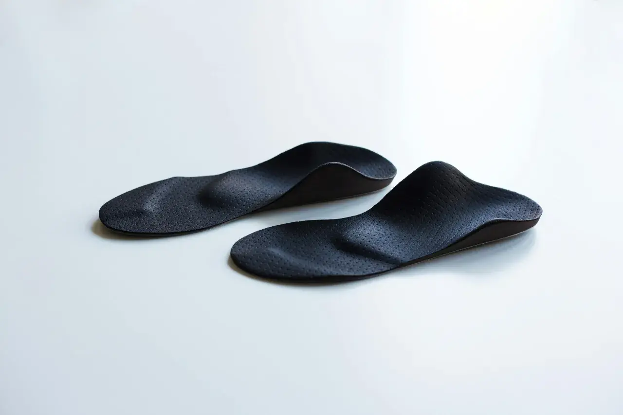 Zwei schwarze, ergonomisch geformte sensomotorische Schuheinlagen liegen auf weißem Untergrund.