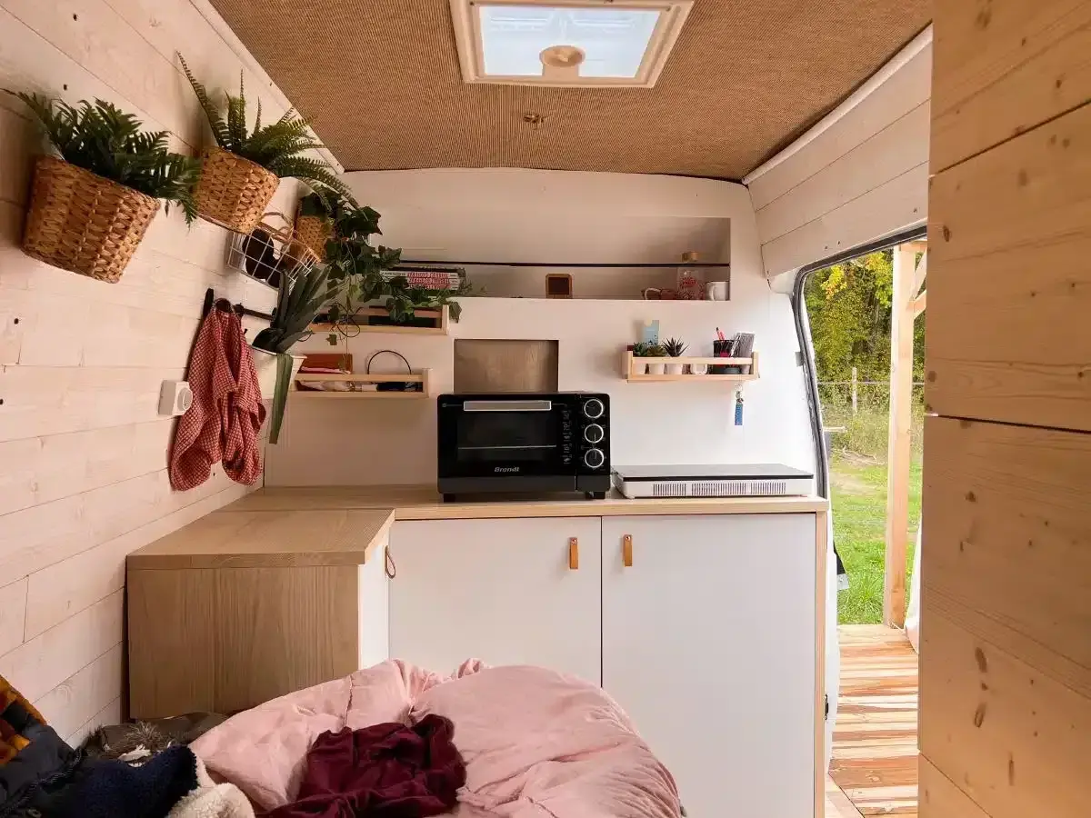 Aménagement intérieur d'un van aménagé : cuisine fonctionnelle avec four, plaque de cuisson, rangements et touches végétales.