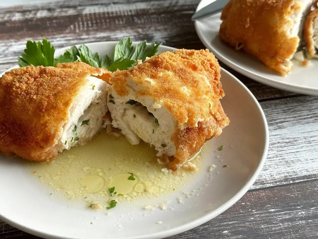Złocisty kotlet de volaille, przekrojony na pół, odsłaniający soczyste wnętrze z ziołami, pływa w maśle.