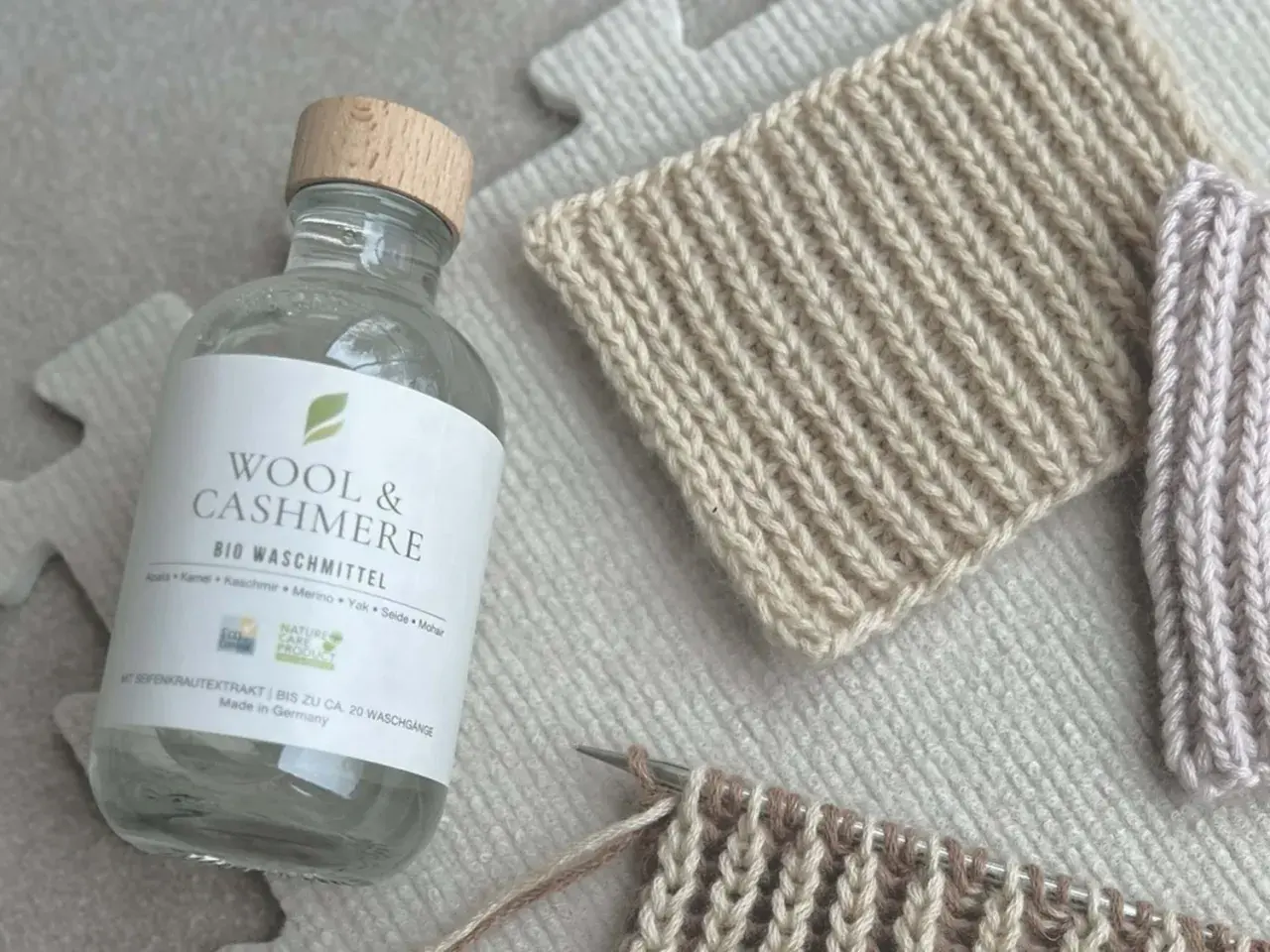 Flasche "Wool & Cashmere" Bio-Waschmittel neben gestrickten Proben. Ideal für die Frage: Pullover waschen welches Programm?