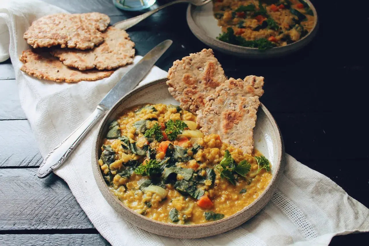 Un plat réconfortant de lentille corail recette, garni de persil frais et servi avec des galettes croustillantes.