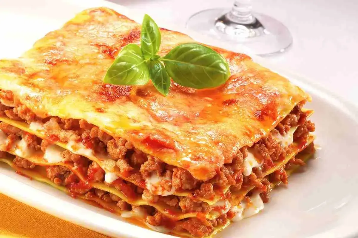 Porzione di lasagne fatte in casa, stratificate con ragù e besciamella, guarnite con basilico fresco.