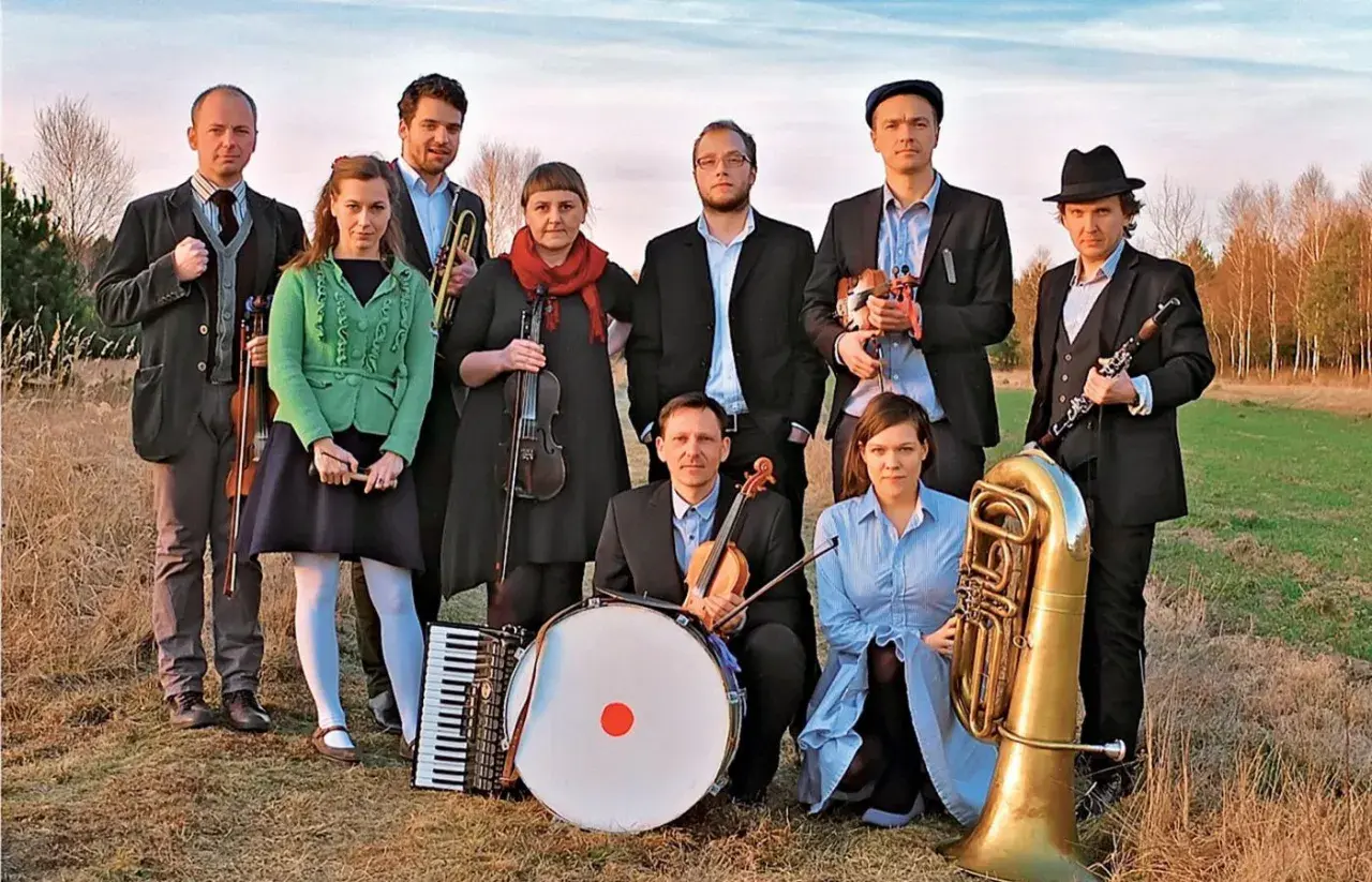 Zespół muzyczny w strojach nawiązujących do stylu folk, z instrumentami: skrzypce, akordeon, bęben, trąbka, klarnet i tuba.