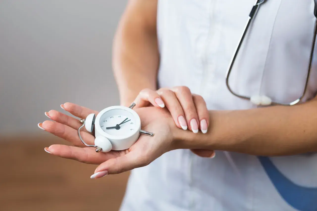 Manos de profesional de la salud sostienen un reloj despertador, simbolizando la presión de trabajo y la importancia del tiempo en la atención médica.