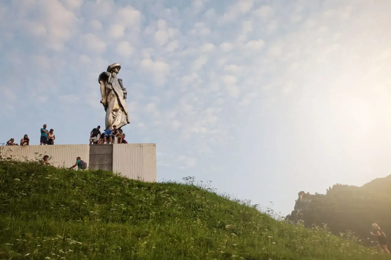 Pomnik Janosika góruje nad wzgórzem, a pod nim siedzą ludzie.