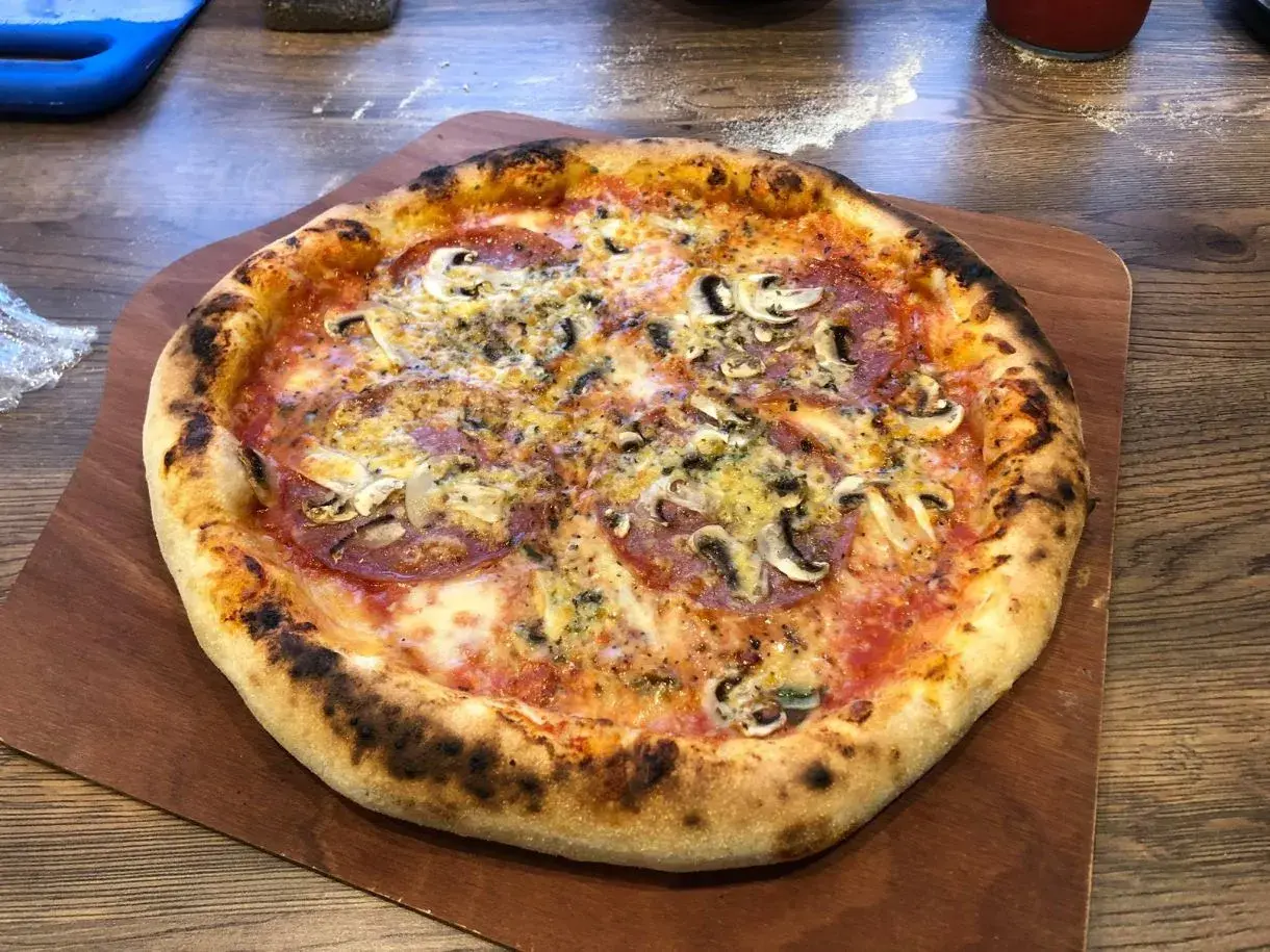 Chrupiąca pizza z pieczarkami i salami na drewnianej desce.