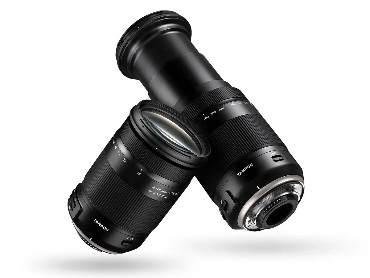 Dwa obiektywy Tamron 18-400 mm, jeden z wysuniętym zoomem, drugi z zasuniętym, unoszą się na białym tle.