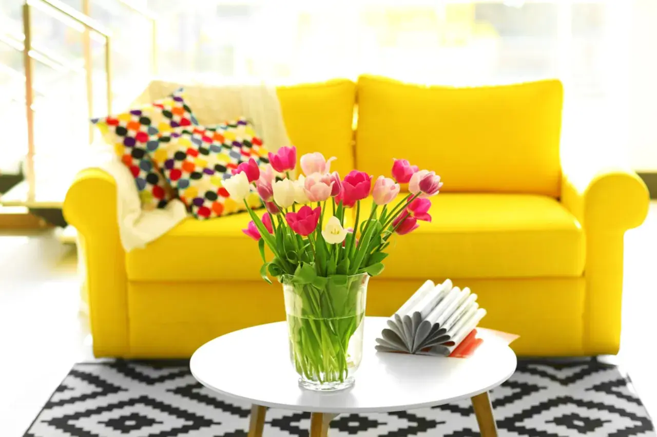 Ein gelbes Sofa mit bunten Kissen und Tulpen auf einem Beistelltisch. Diese stilvolle Deko im Wohnzimmer strahlt Fröhlichkeit aus.