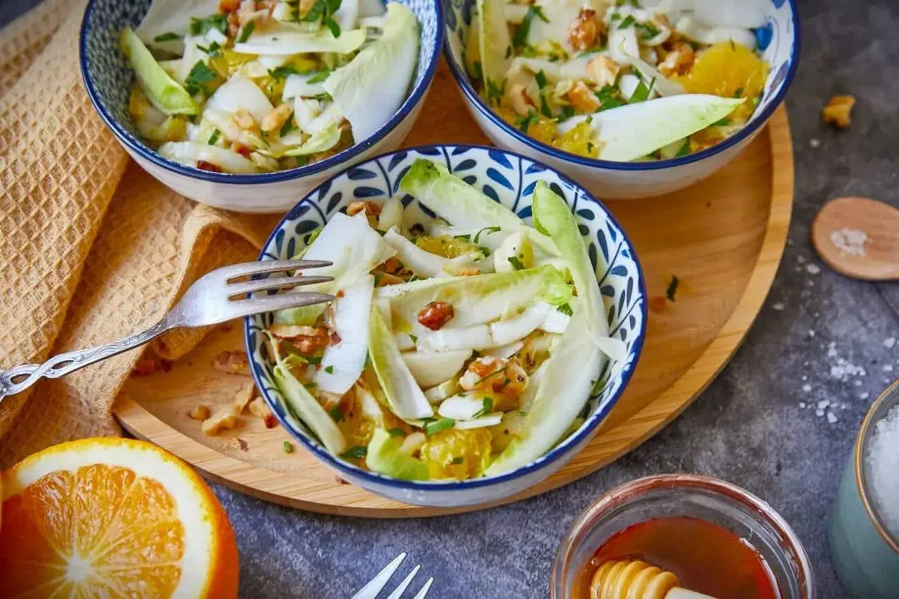 Erfrischender Chicorée-Salat mit Orangenstücken und Nüssen in blauen Schalen, serviert auf einem Holztablett.