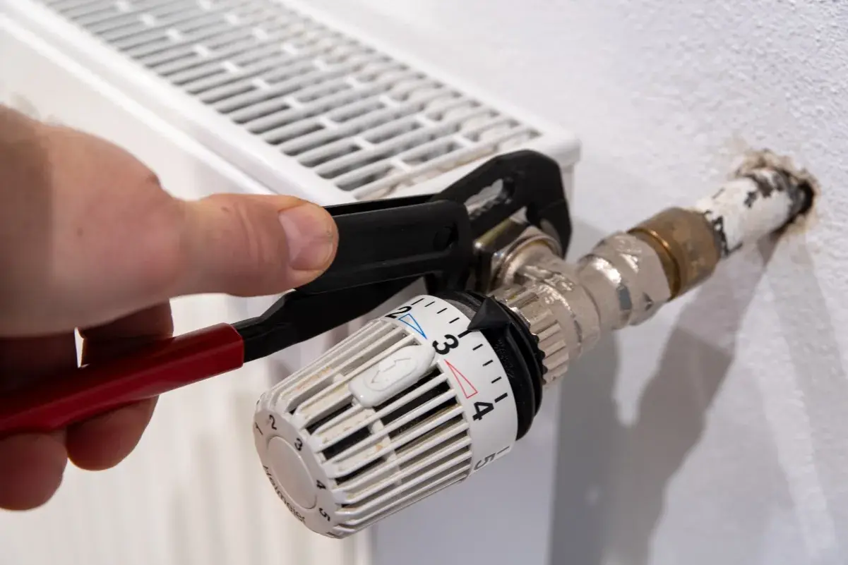 Hand uses pliers to heizungsventil tauschen. Der Thermostatkopf ist auf Stufe 3 eingestellt.