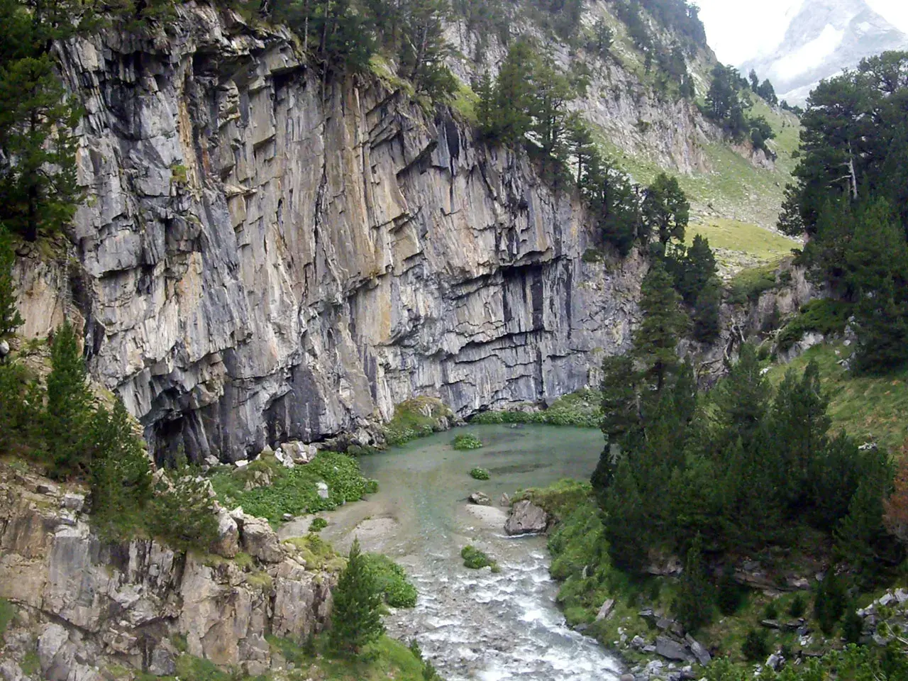 Impresionante pared rocosa junto a un río y vegetación exuberante en el forau de Aigualluts.