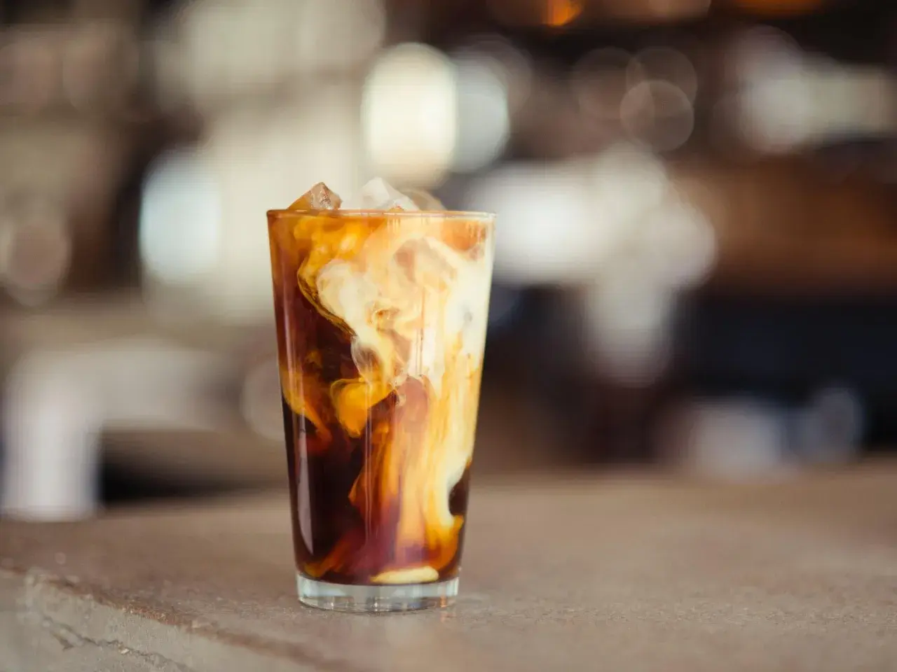 Ein Glas Eiskaffee mit Milchwirbeln und Eiswürfeln. Perfekt für ein iced coffee rezept schnell an heißen Tagen.