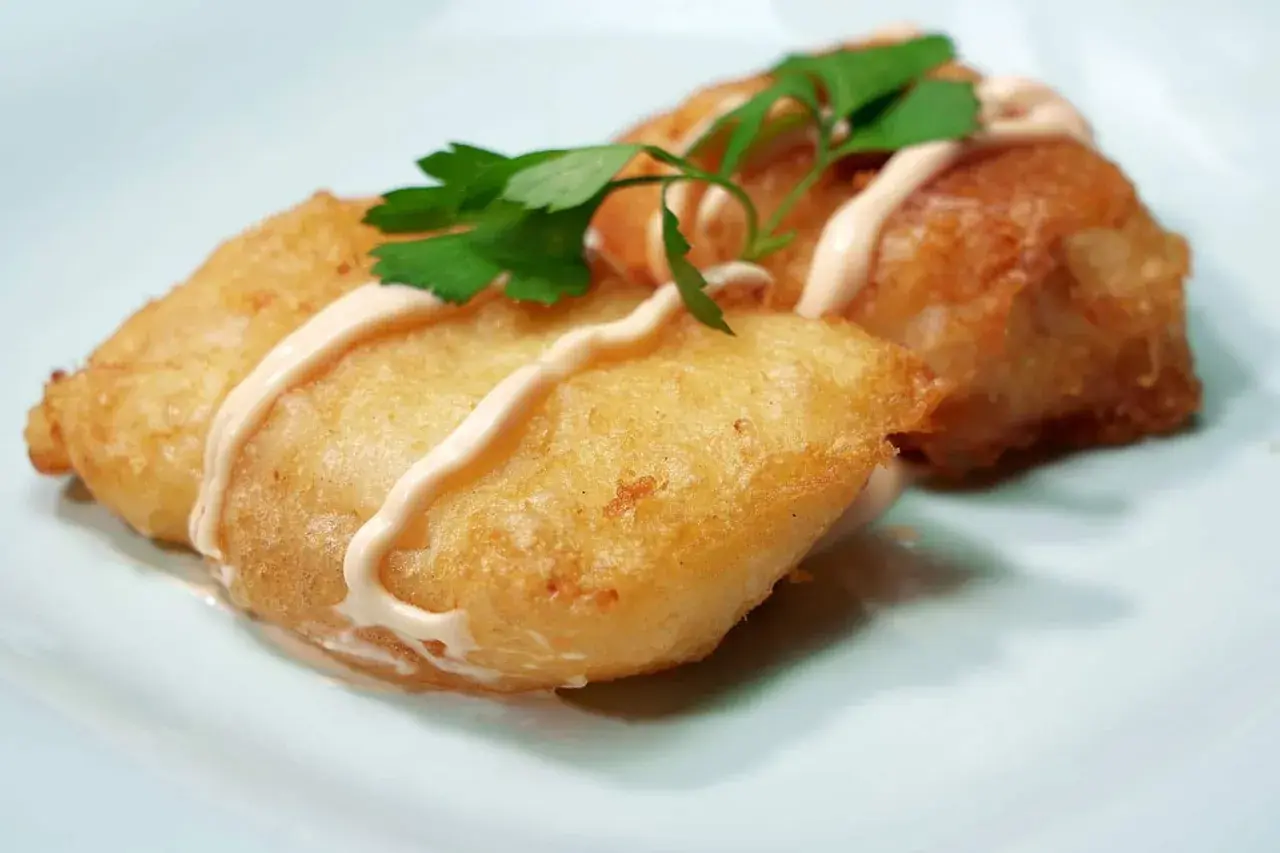 Dos trozos de bacalao rebozado, dorados y crujientes, servidos con una salsa cremosa y perejil fresco.