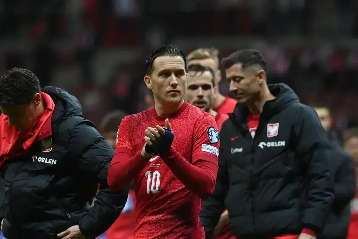 Piłkarze reprezentacji Polski, w tym Lewandowski, w czerwonych strojach i czarnych kurtkach, z nadzieją patrzą w przyszłość, marząc o baraze ms 2026.