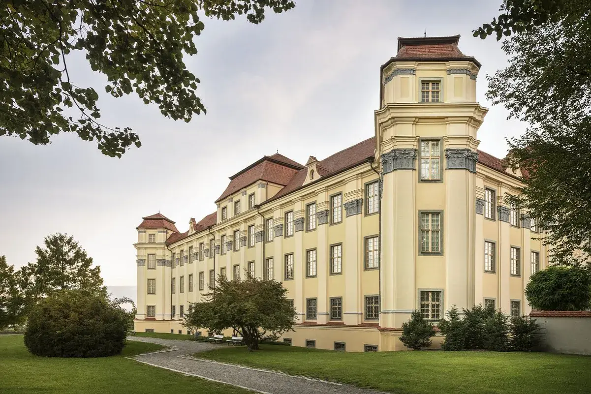 Das neue Schloss Tettnang erstrahlt in hellem Gelb mit roten Dächern. Ein Weg führt durch den gepflegten Garten.