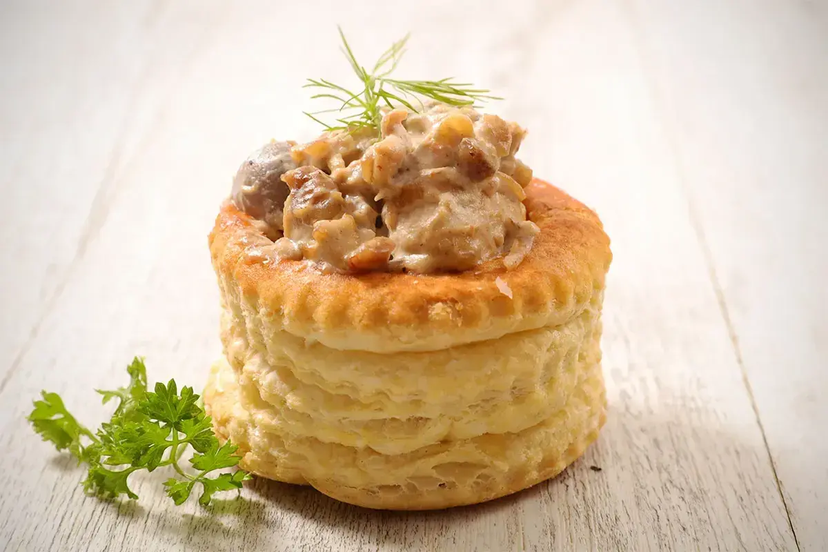 Une délicieuse bouchée à la reine, garnie d'une sauce crémeuse aux champignons et volaille, sur fond de bois clair.