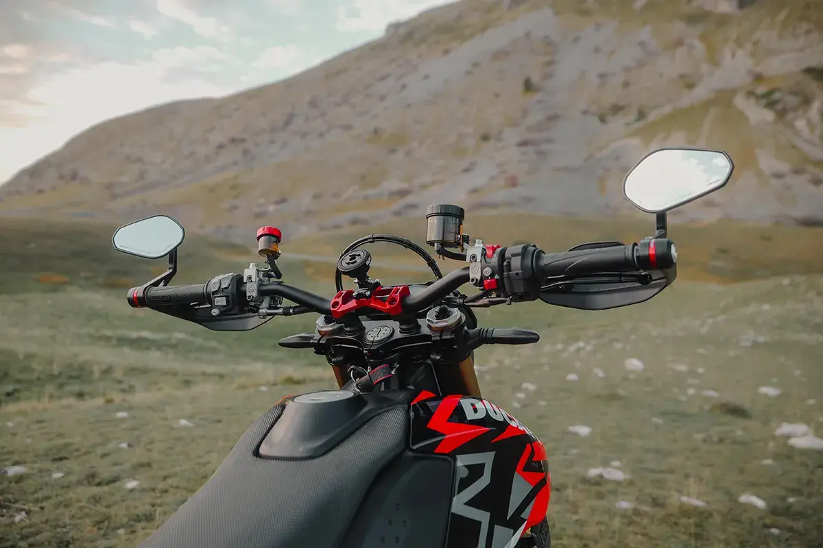Manubrio di una moto con specchietti bar end, pronto per un'avventura tra le montagne.