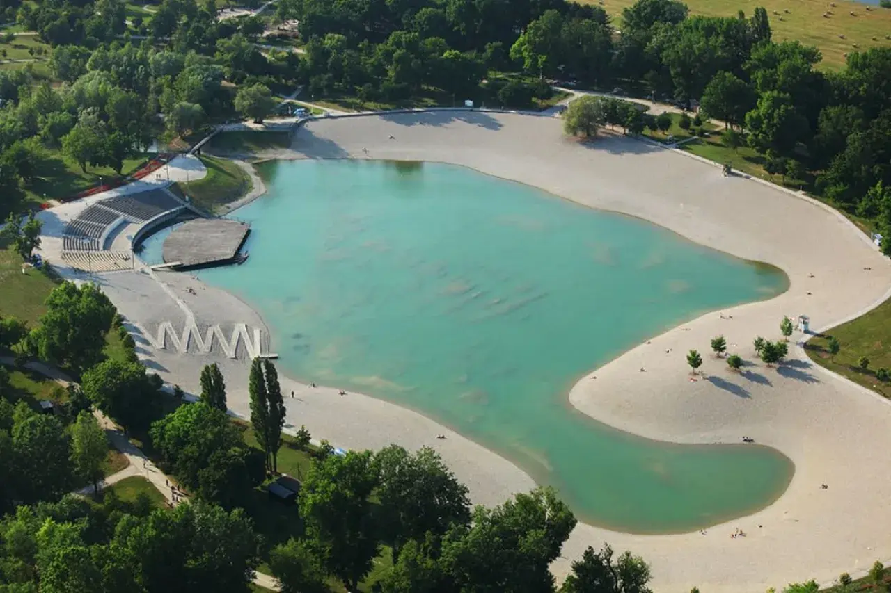 Zagrzeb plaża z turkusową wodą i piaszczystymi brzegami, otoczona zielenią. Widoczne amfiteatr i drewniany pomost.