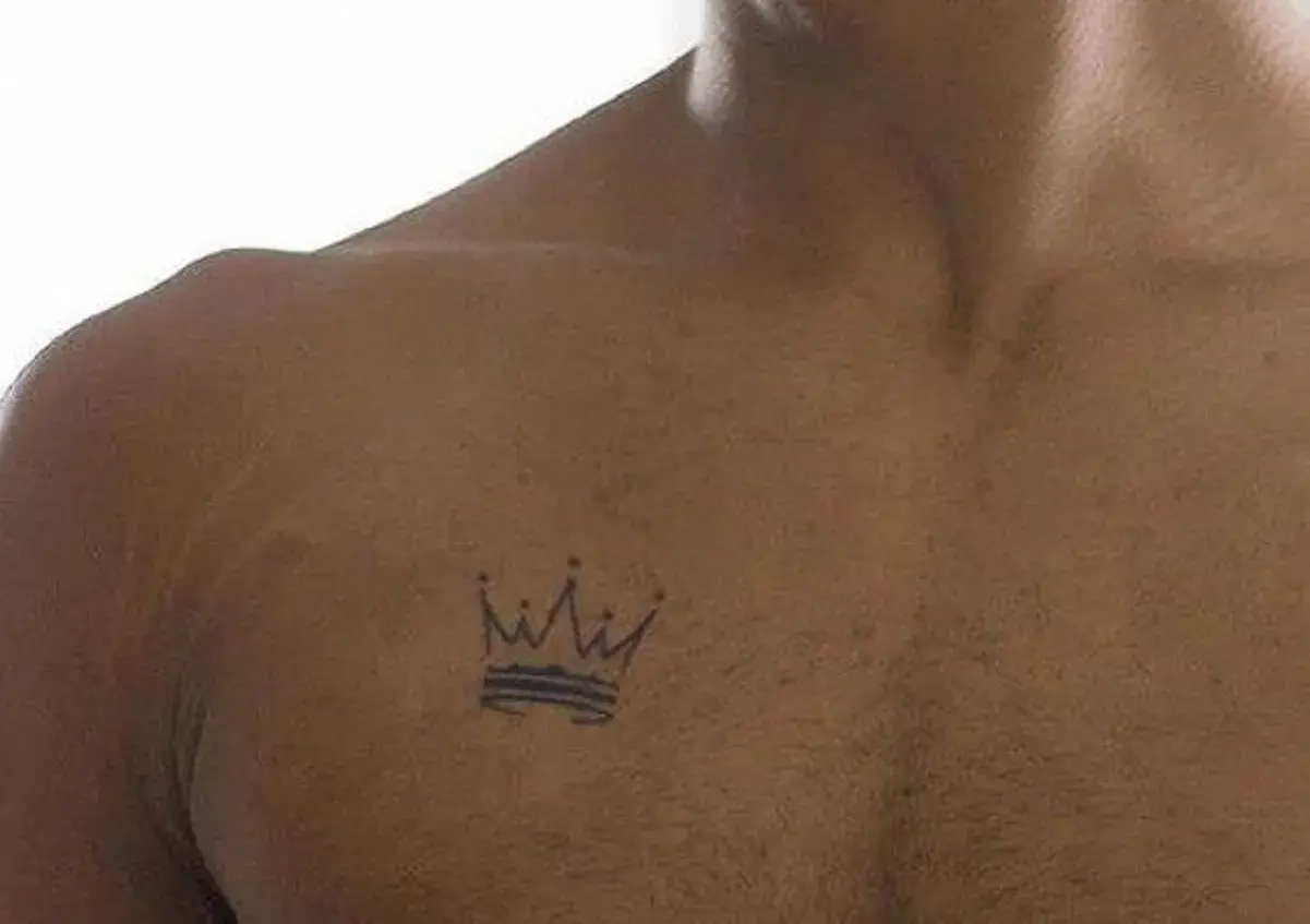 Mały, czarny tatuaż korony na klatce piersiowej. Symbolizuje siłę i władzę, idealny dla króla życia.