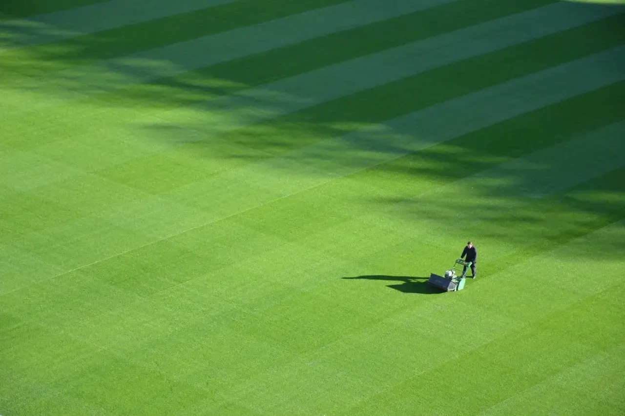 Greenkeeper praca: mężczyzna kosi trawnik na boisku sportowym, tworząc idealne pasy.