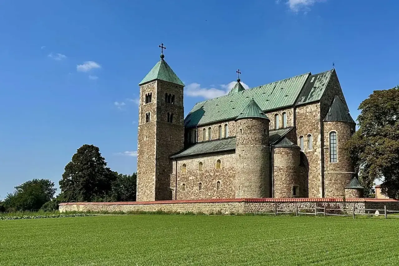 Romańska bazylika tum pod Łęczycą, z zielonymi dachami i kamiennym murem, na tle błękitnego nieba.