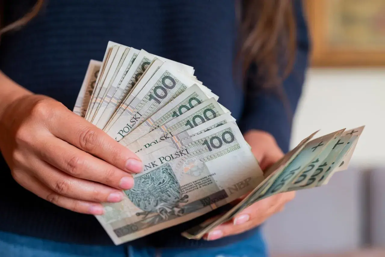 Dłonie trzymające stos banknotów 100 zł. Czy to przedpłata, czy zaliczka? Decyzja o płatności.