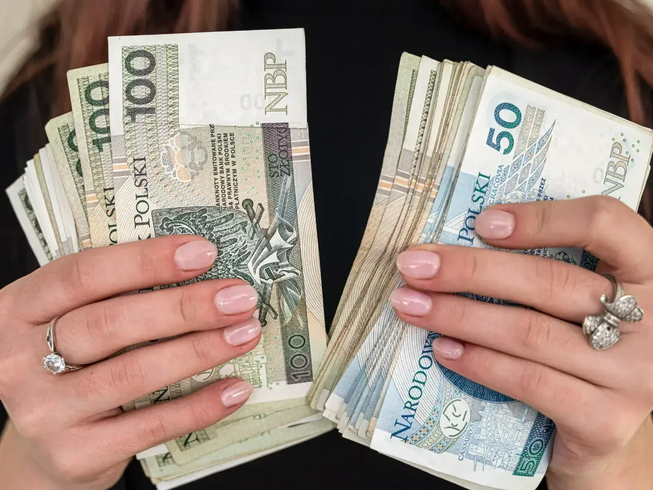 Dłonie z paznokciami pomalowanymi na jasny róż trzymają stosy polskich złotówek. W jednej ręce banknoty 100 zł, w drugiej 50 zł. To pewnie babciowe na drobne wydatki.