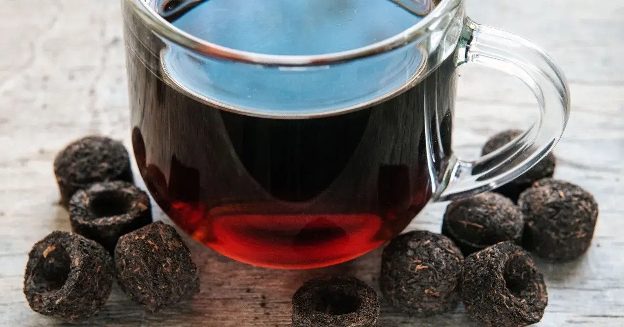 Szklanka z aromatycznym, czerwonym herbatą, otoczona sprasowanymi liśćmi, gotowa do zaparzenia.