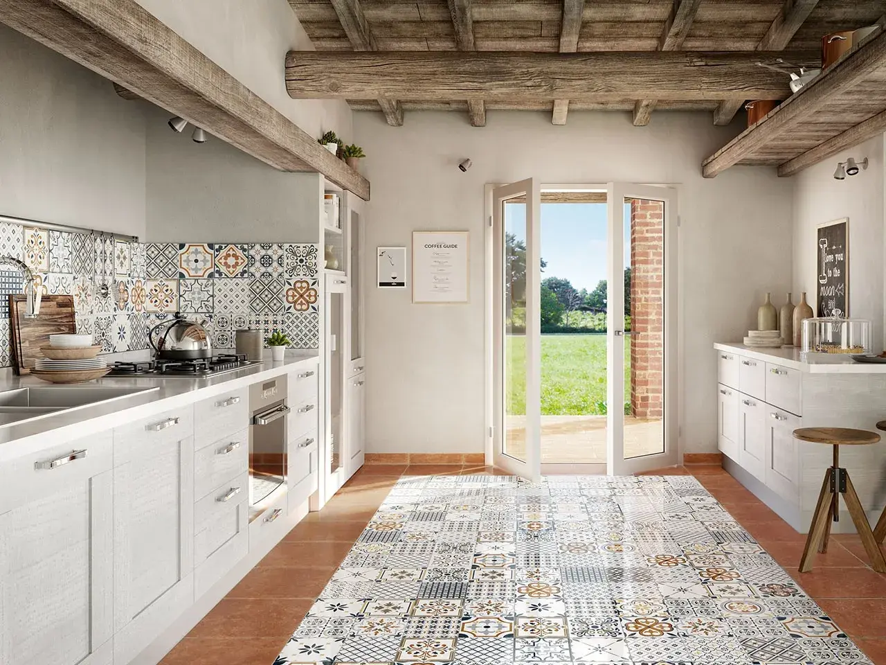 Cucina rustica con pavimento decorato, pensili bianchi e un'ampia porta finestra che si apre su un prato verde. La posa battiscopa è curata nei dettagli.